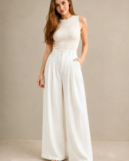 Model wearing white wide-leg trousers in a tencel-linen blend with a draped finish and pleated high waist, styled with an ivory ribbed tank top, front view.