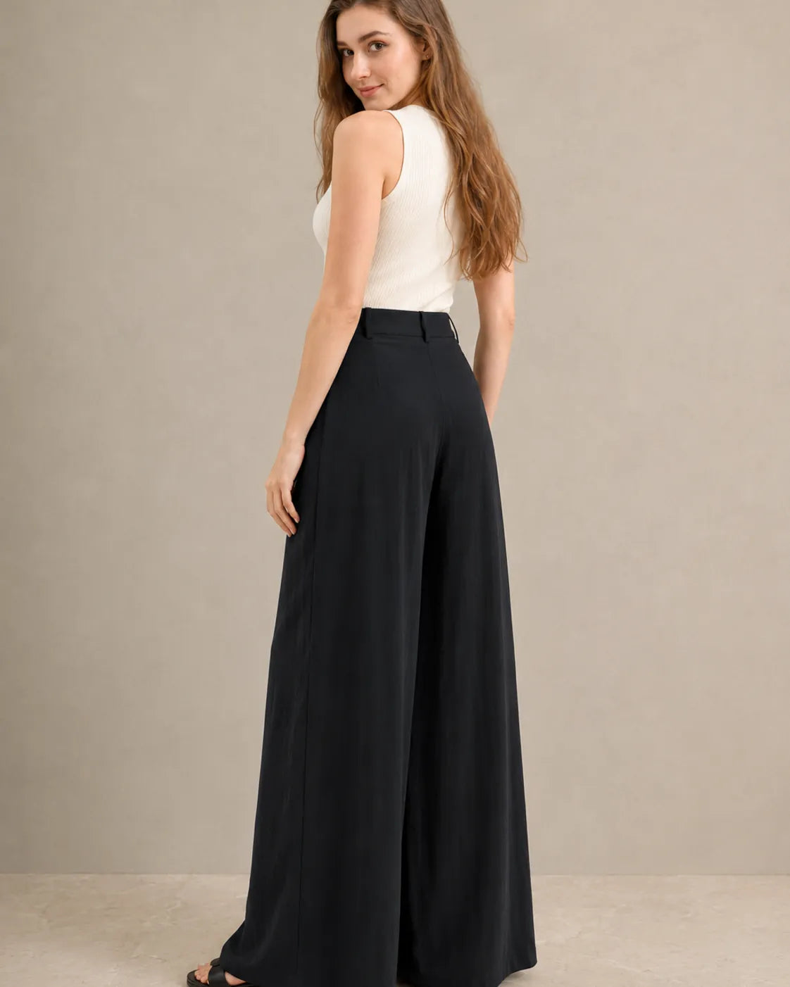 Three-quarter back view of model wearing black wide-leg trousers in a tencel-linen blend with a draped finish.