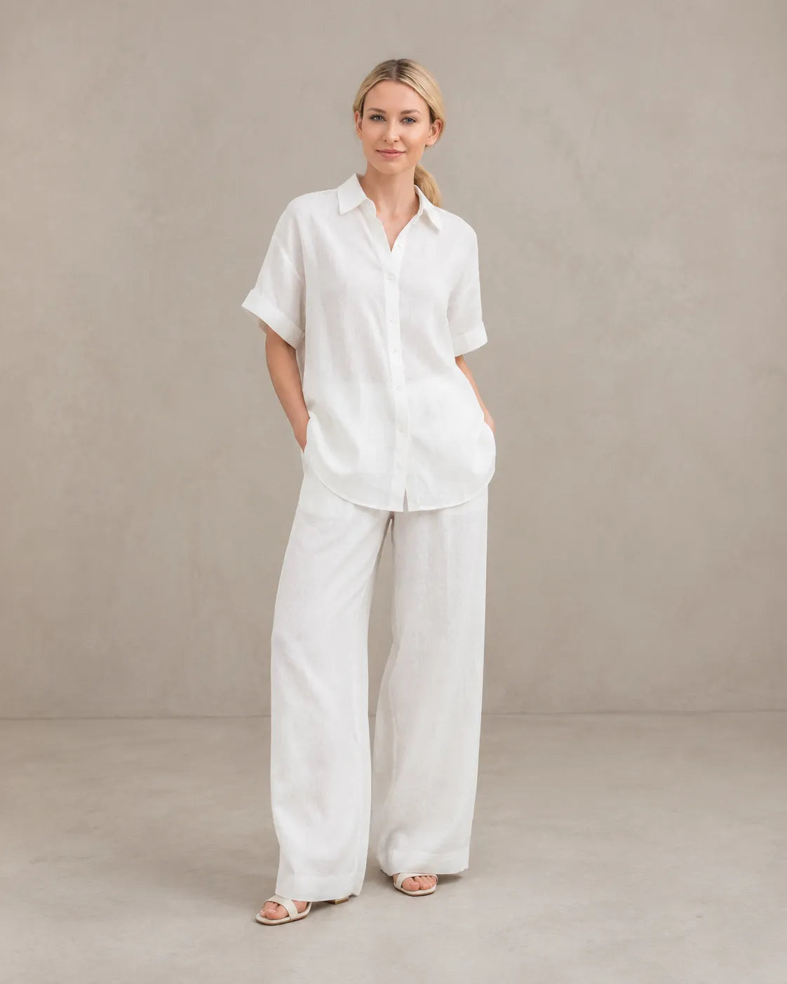 Een model draagt de witte cardigan-achtige top en wijde broek, staand in een ontspannen vooraanzicht.