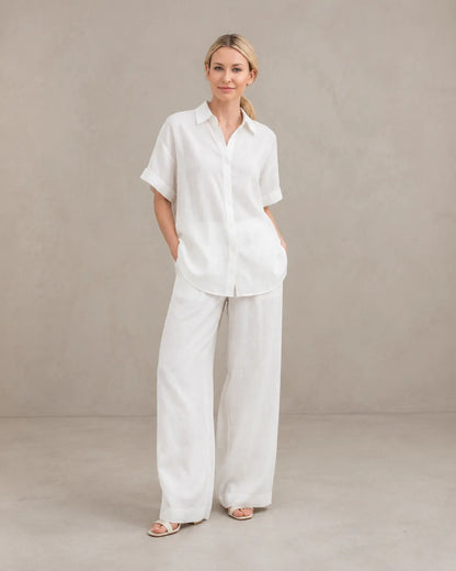 Een model draagt de witte cardigan-achtige top en wijde broek, staand in een ontspannen vooraanzicht.