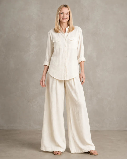 Een dichterbij vooraanzicht van een model in de linnen co-ord set in beige-wit, met een blouse met borstzakken en een wijde broek.