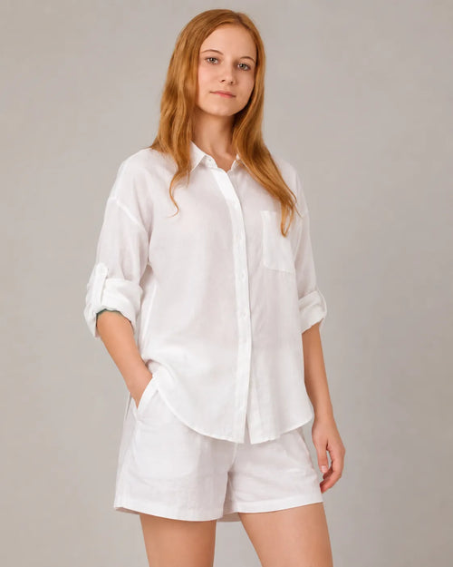 A model wears the linen-cotton co-ord set in white, turned to show the button-down shirt with a chest pocket and matching shorts.