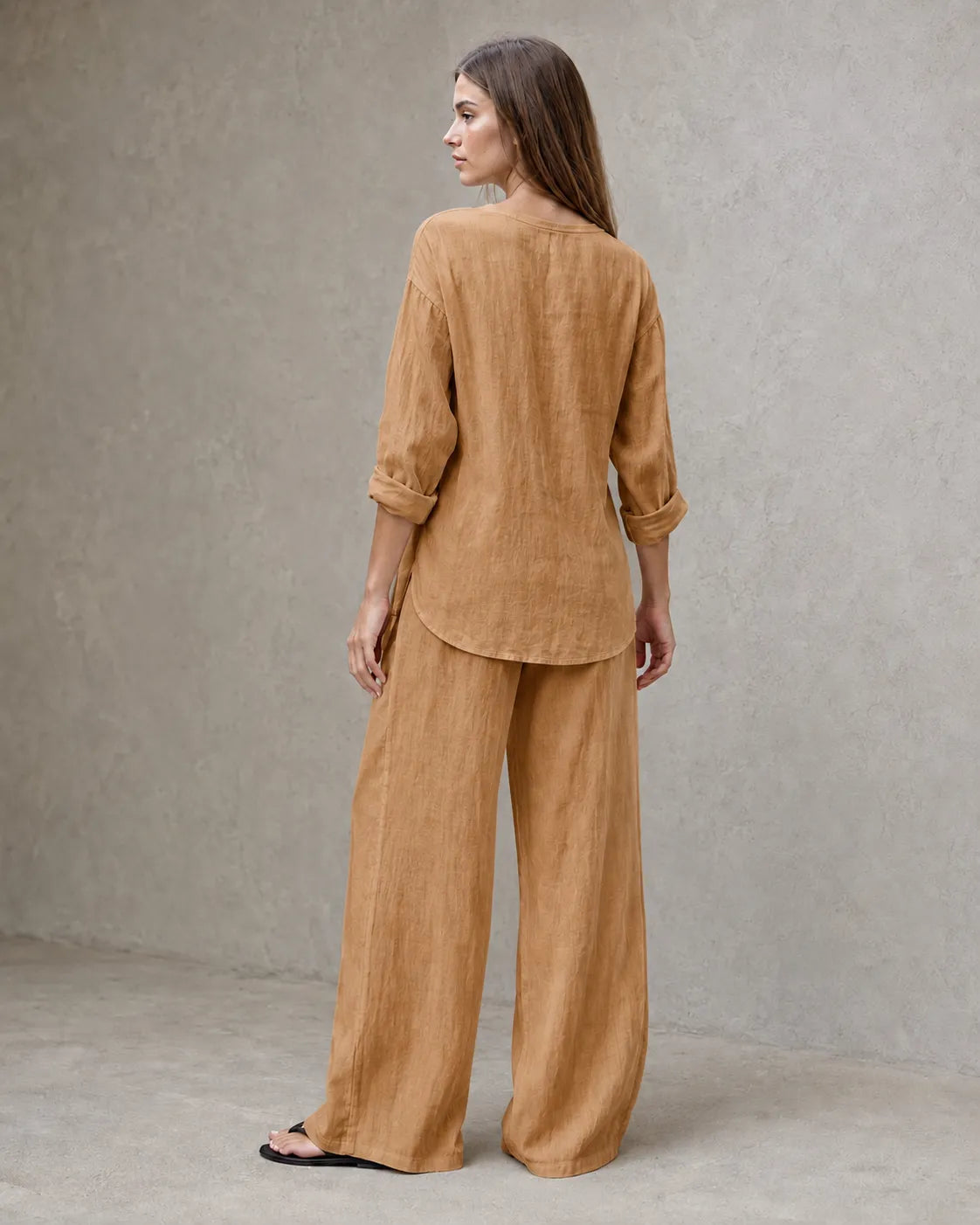 Achteraanzicht van een model in de camelkleurige linnenmix co-ord set met V-hals, met de tuniektop vallend over de geplooide broek.