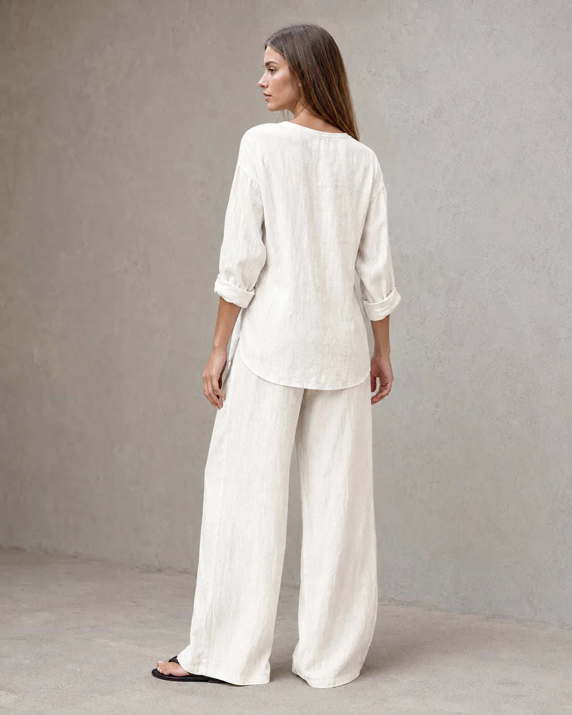 Achteraanzicht van een model in de gebroken witte linnenmix co-ord set met V-hals, met de tuniektop vallend over de geplooide broek.