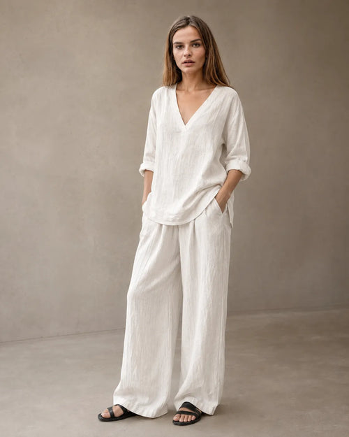 Een model draagt de linnenmix co-ord set met V-hals in gebroken wit, met een tuniektop met lange mouwen en een bijpassende geplooide wijde broek.