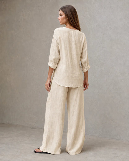 Achteraanzicht van een model in de zandkleurige linnenmix co-ord set met V-hals, met de tuniektop vallend over de geplooide broek.