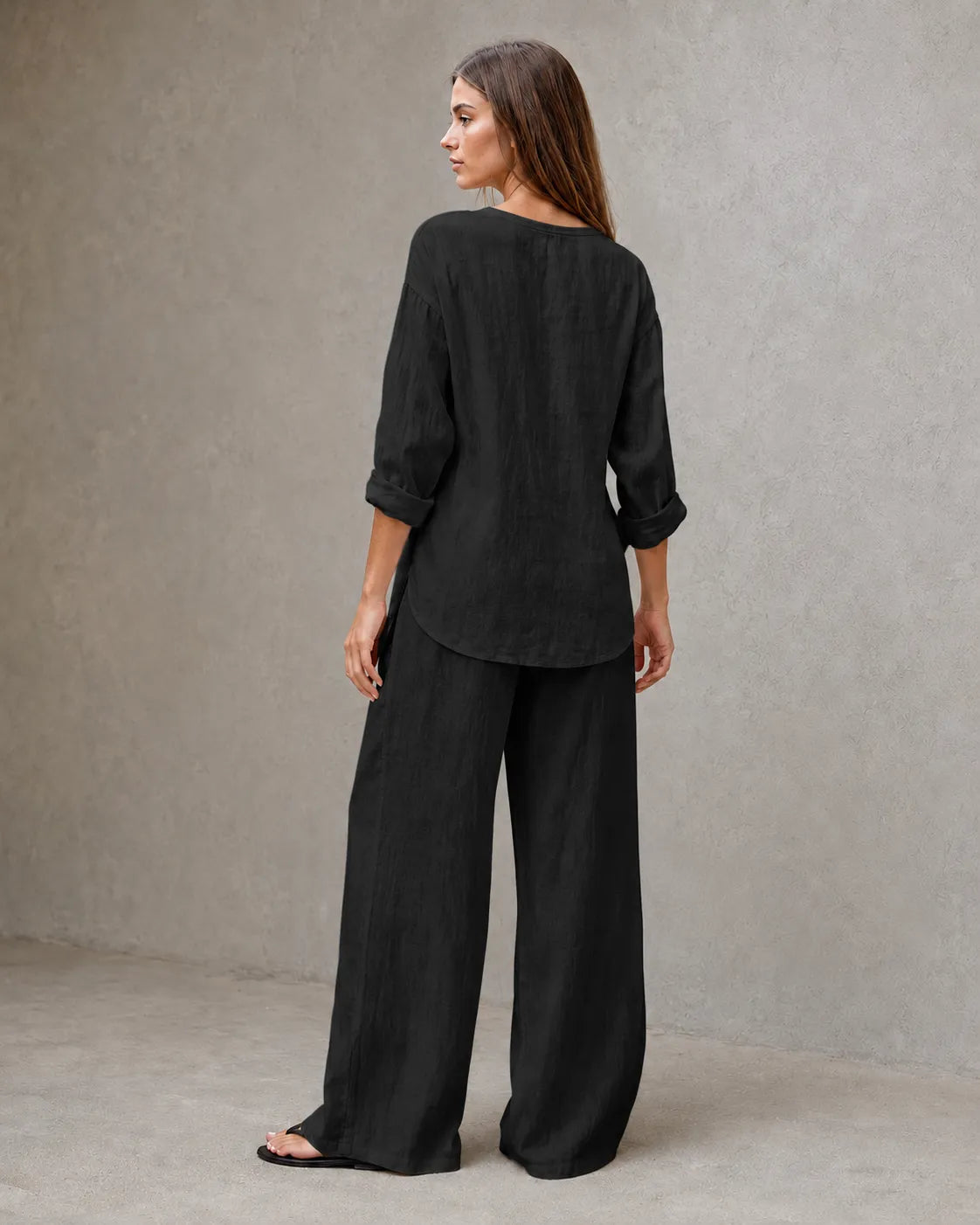 Achteraanzicht van een model in de zwarte linnenmix co-ord set met V-hals, met de tuniektop vallend over de geplooide broek.