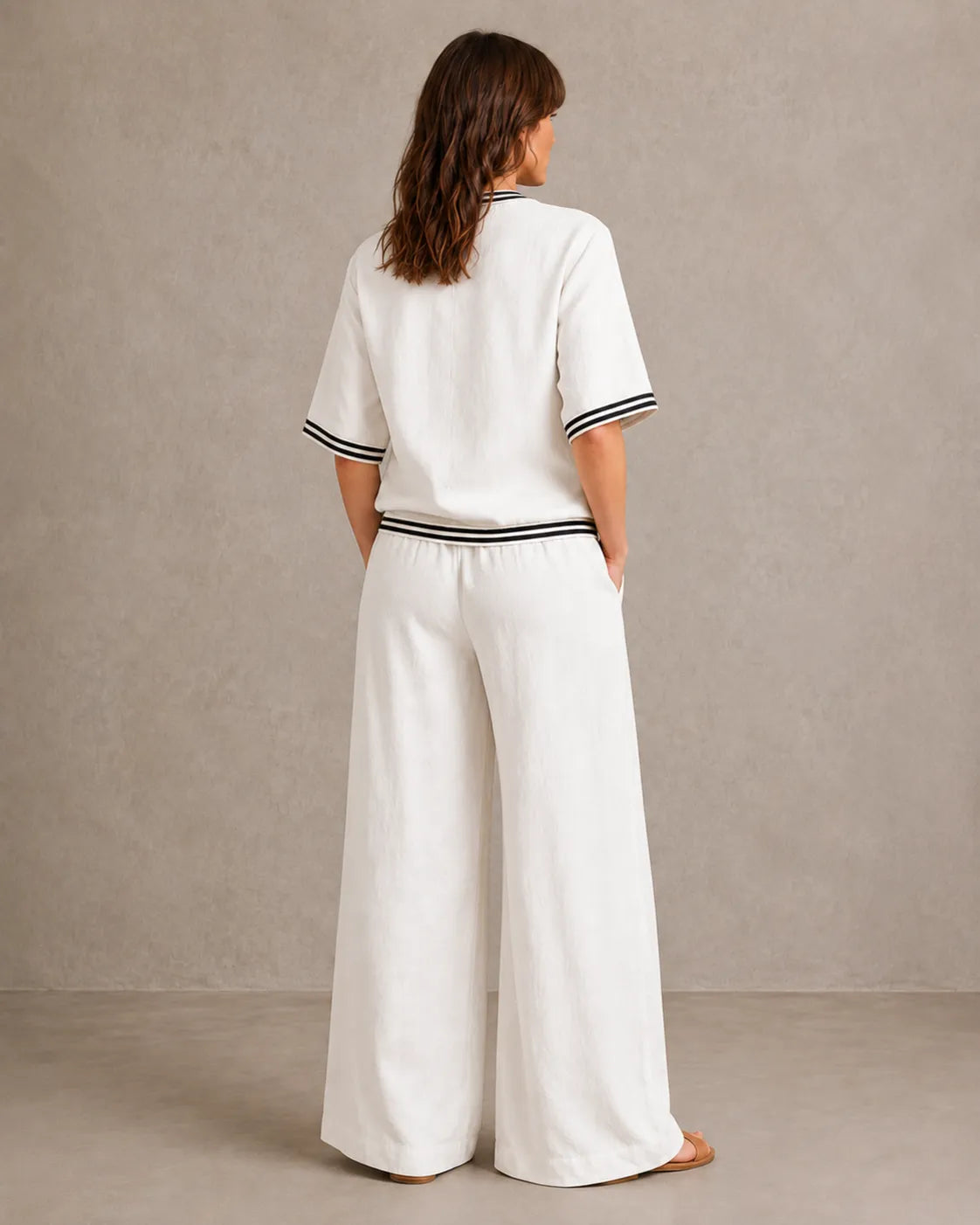Achteraanzicht van een model in de melkwitte linnen co-ord set met V-hals, met de gestreepte taille en wijde broek.