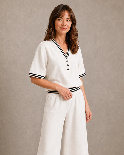 Een model in de melkwitte linnen co-ord set met V-hals, gedraaid om de gestreepte halsboord en knoopsluiting dichterbij te tonen.