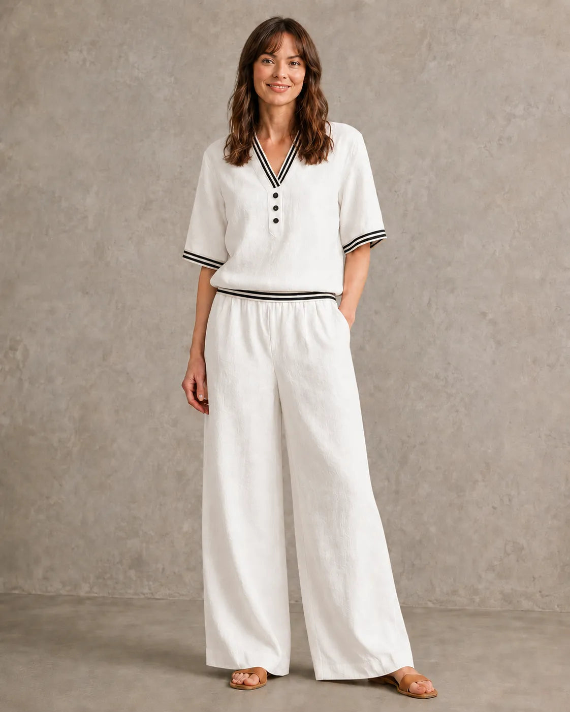 Een model draagt de linnen co-ord set met V-hals in melkwit, met een top met gestreepte boorden en een bijpassende wijde broek.