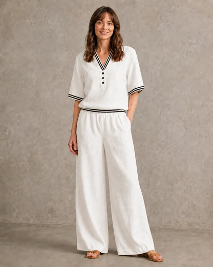 Een model draagt de linnen co-ord set met V-hals in melkwit, met een top met gestreepte boorden en een bijpassende wijde broek.