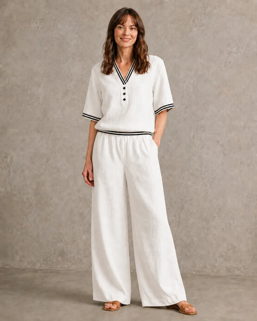 Een model draagt de linnen co-ord set met V-hals in melkwit, met een top met gestreepte boorden en een bijpassende wijde broek.