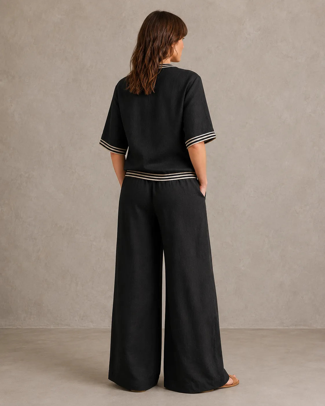 Achteraanzicht van een model in de zwarte linnen co-ord set met V-hals, met de gestreepte taille en wijde broek.