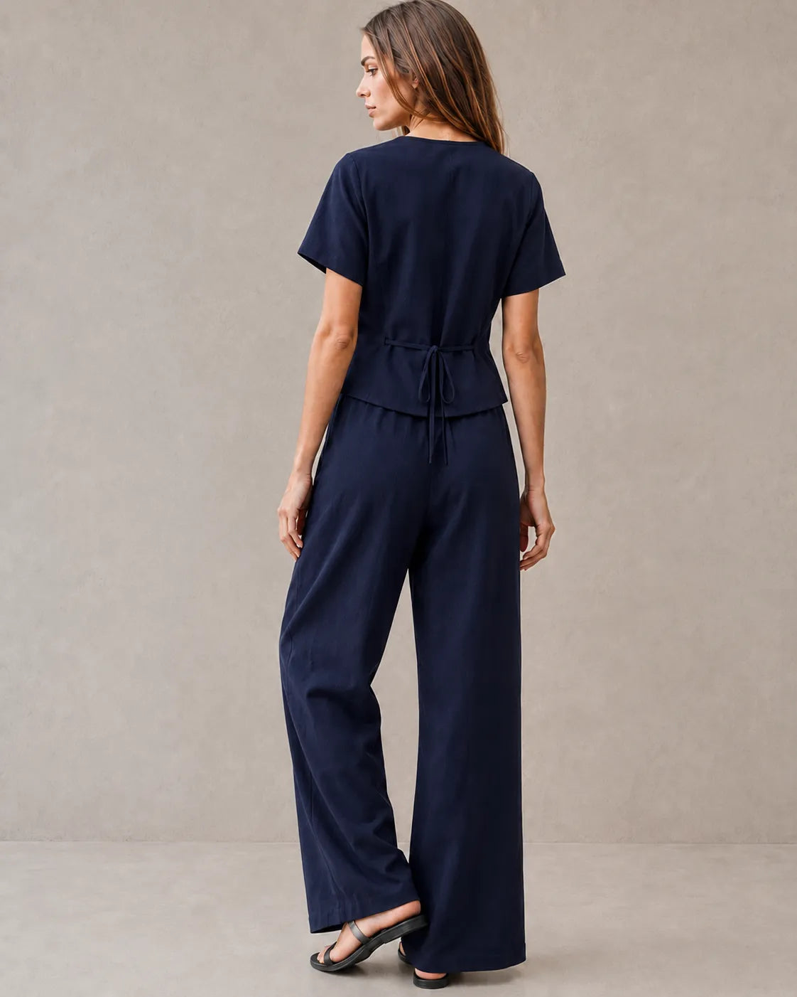 Achteraanzicht van een model in de marineblauwe tencel-linnen co-ord set, met de strikceintuur aan de achterkant van de top en de wijde broek.