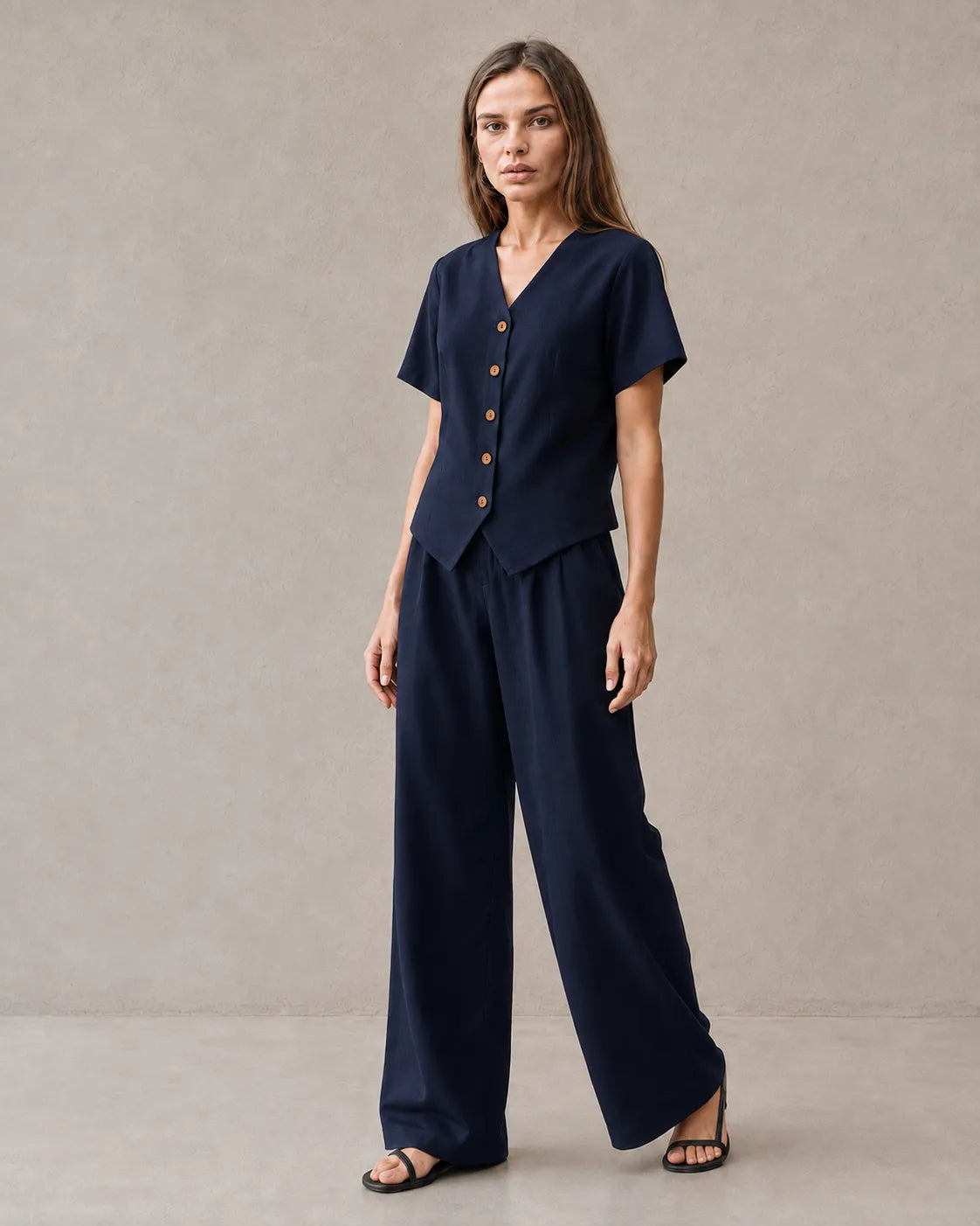 Een model draagt de tencel-linnen co-ord set in marineblauw, met een top met korte mouwen, V-hals en knoopsluiting, en een bijpassende wijde broek.