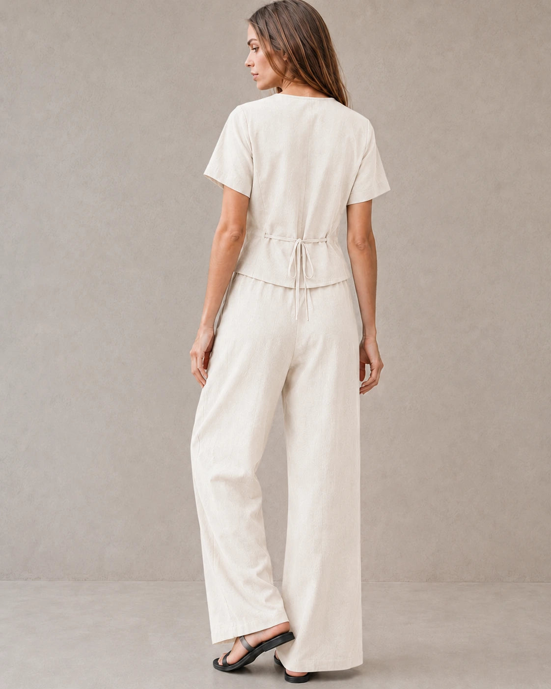 Achteraanzicht van een model in de off-white tencel-linnen co-ord set, met de strikceintuur aan de achterkant van de top en de wijde broek.