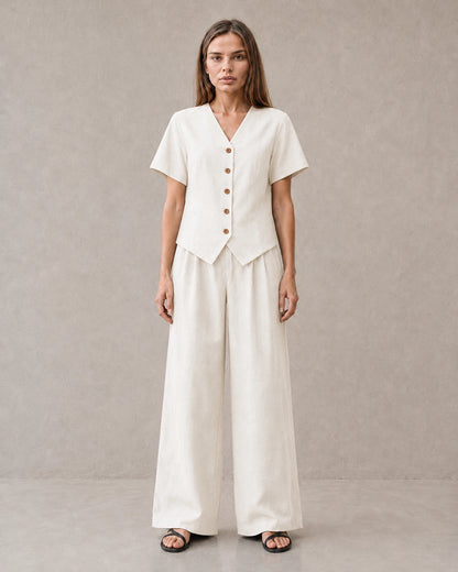 Een dichterbij vooraanzicht van een model in de off-white tencel-linnen co-ord set, met de V-hals en knoopsluiting van de top.