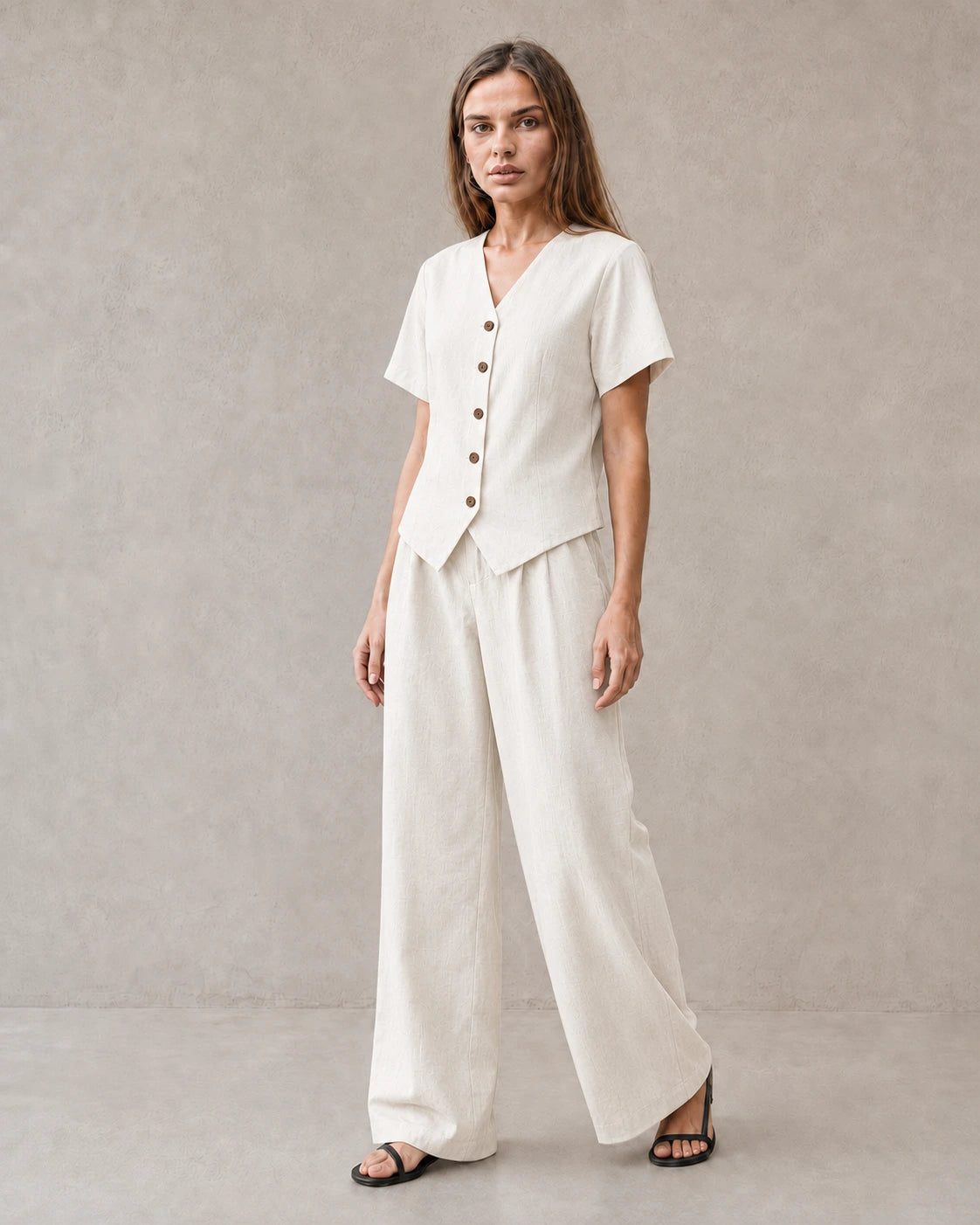 Een model draagt de tencel-linnen co-ord set in off-white, met een top met korte mouwen, V-hals en knoopsluiting, en een bijpassende wijde broek.