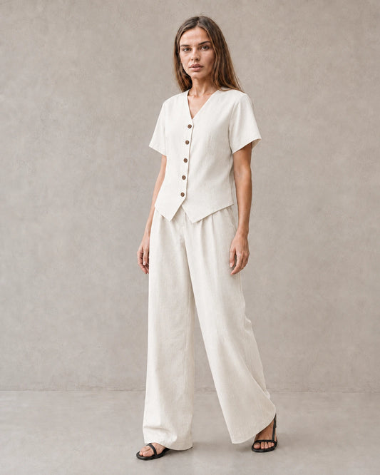 Een model draagt de tencel-linnen co-ord set in off-white, met een top met korte mouwen, V-hals en knoopsluiting, en een bijpassende wijde broek.