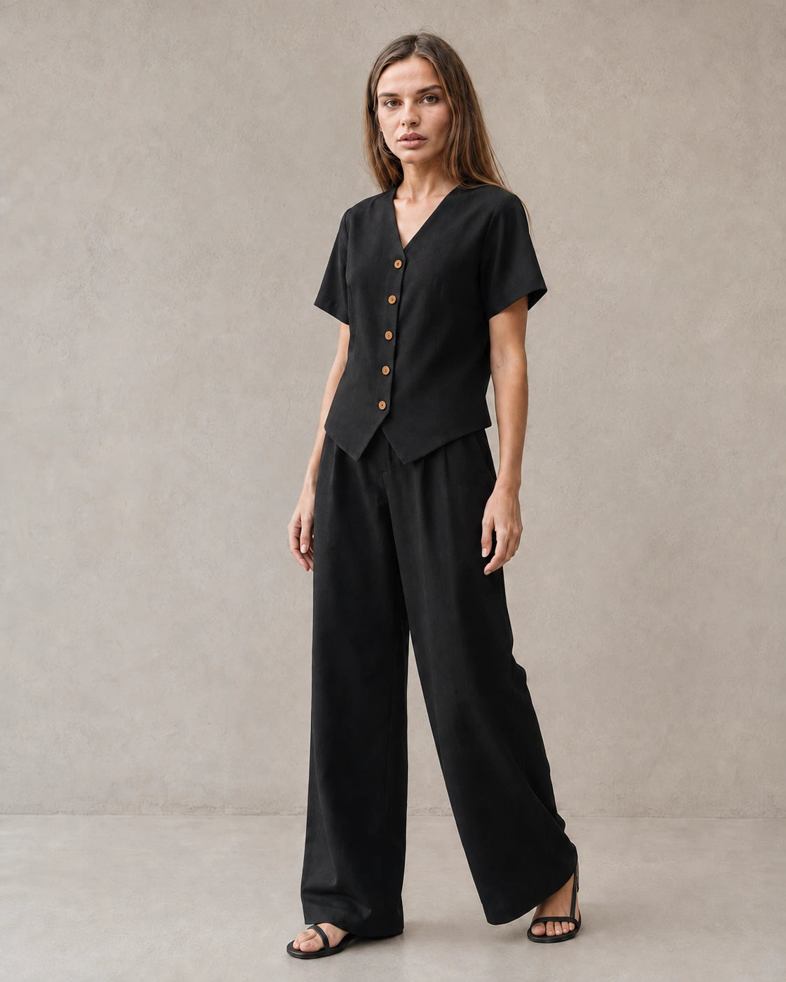 Een model draagt de tencel-linnen co-ord set in zwart, met een top met korte mouwen, V-hals en knoopsluiting, en een bijpassende wijde broek.
