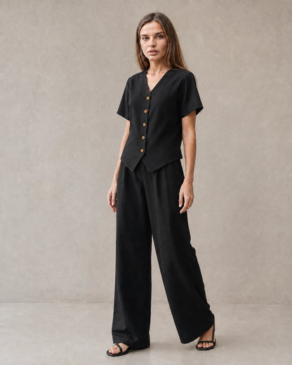 Een model draagt de tencel-linnen co-ord set in zwart, met een top met korte mouwen, V-hals en knoopsluiting, en een bijpassende wijde broek.
