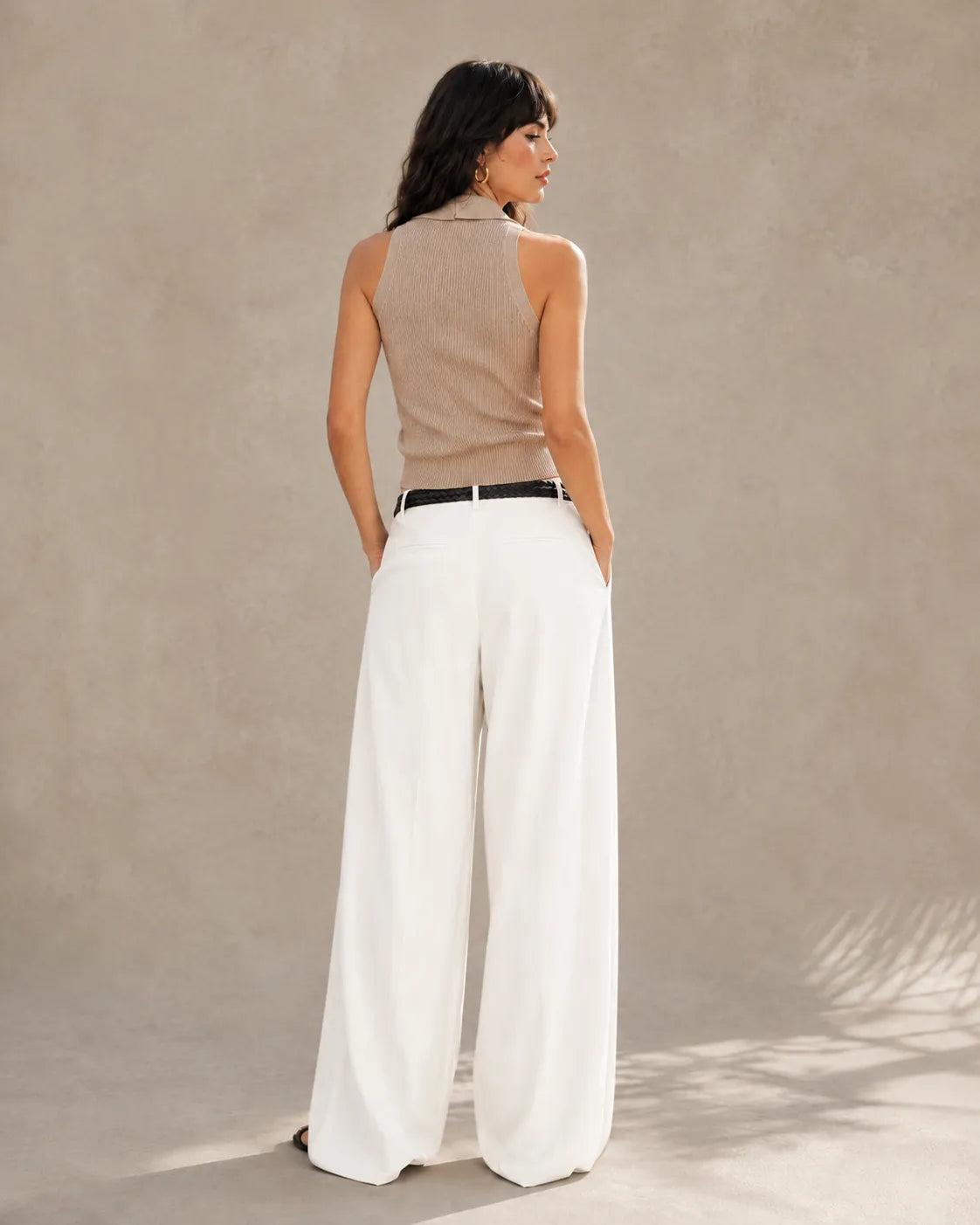 Back view of a woman wearing pearl white tencel-linen wide-leg trousers with a high waist.