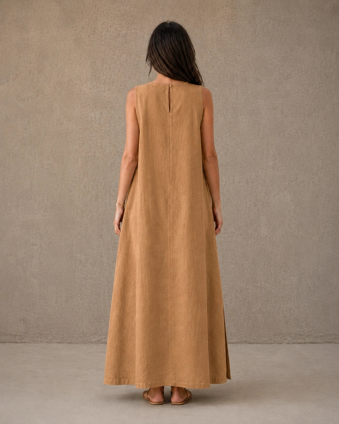 Achteraanzicht van een mouwloze linnen A-lijn jurk in camel met knoopsluiting bij de hals, gedragen door een model.
