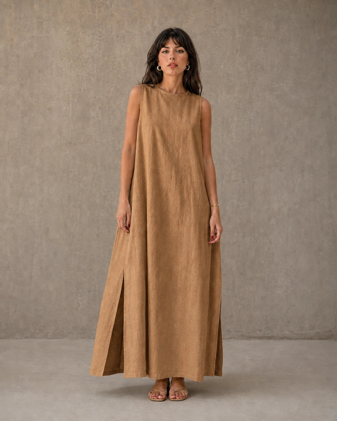 Vrouw draagt een mouwloze linnen A-lijn jurk in camel met ronde hals en splits in de zijzoom, vooraanzicht.