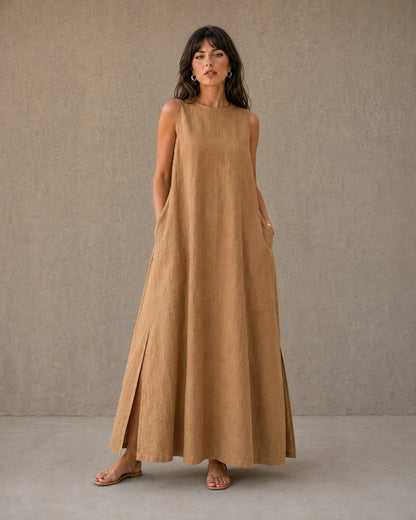 Vrouw draagt een mouwloze linnen A-lijn jurk in camel, met zicht op de splits in de zijzoom, vooraanzicht.