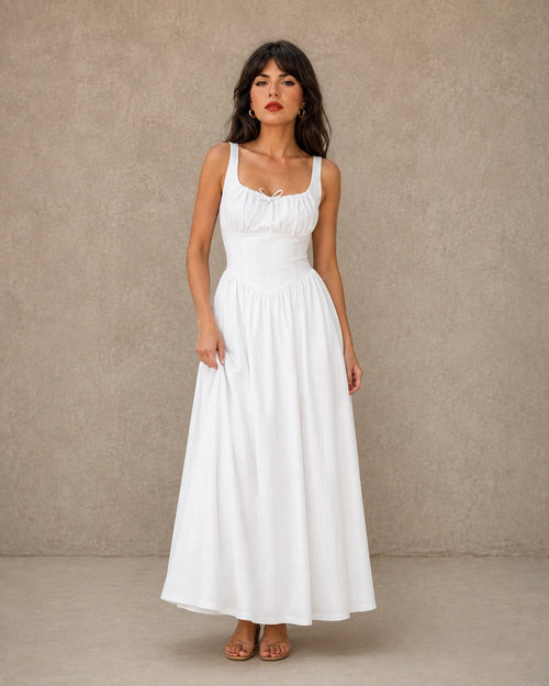Vrouw draagt een linnen jurk in wit met een getailleerd, geplooid lijfje, strikdetail bij de hals en een volle A-lijn rok, vooraanzicht.