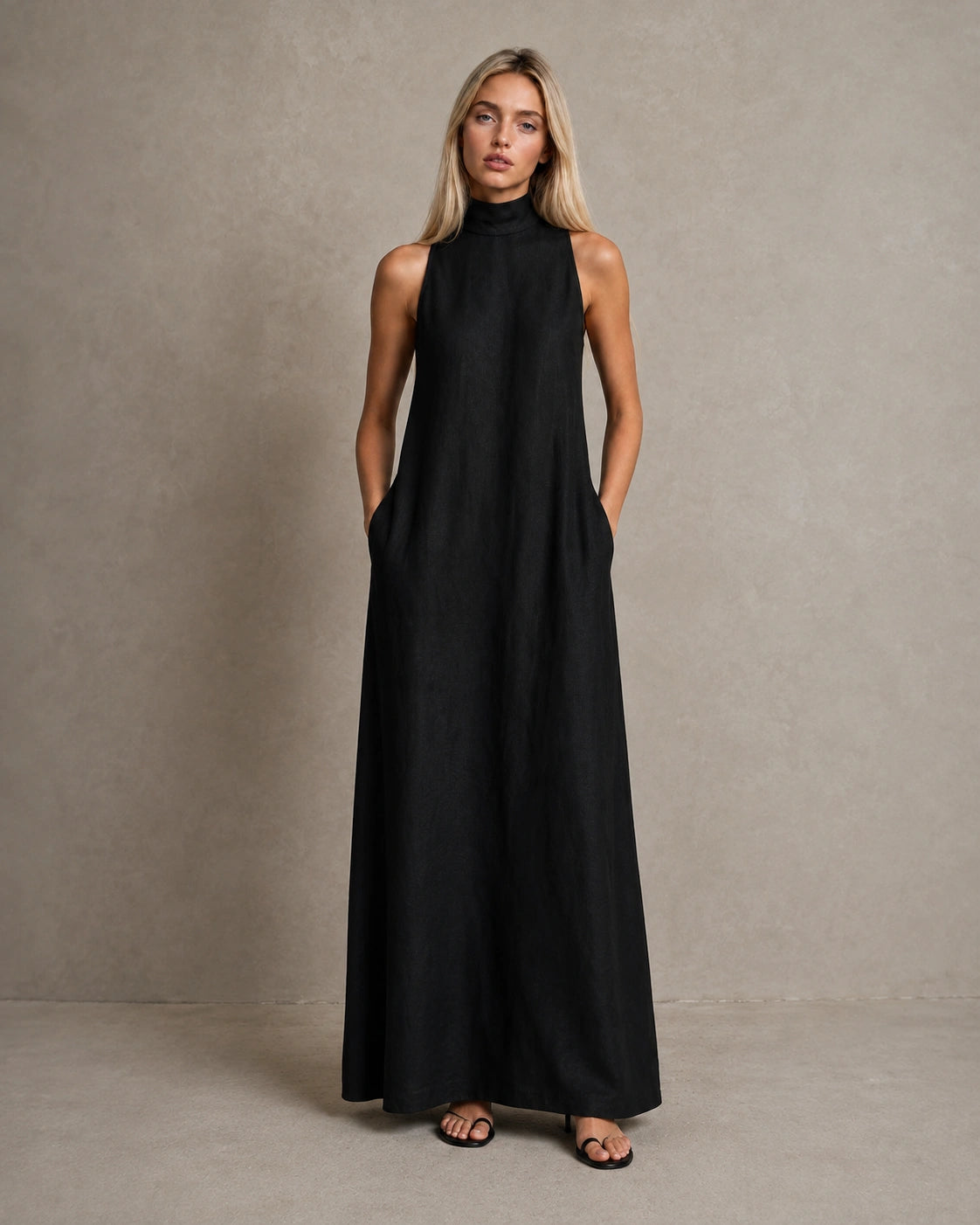 Vrouw draagt een linnen A-lijn jurk in zwart met hoge hals en steekzakken, vooraanzicht.