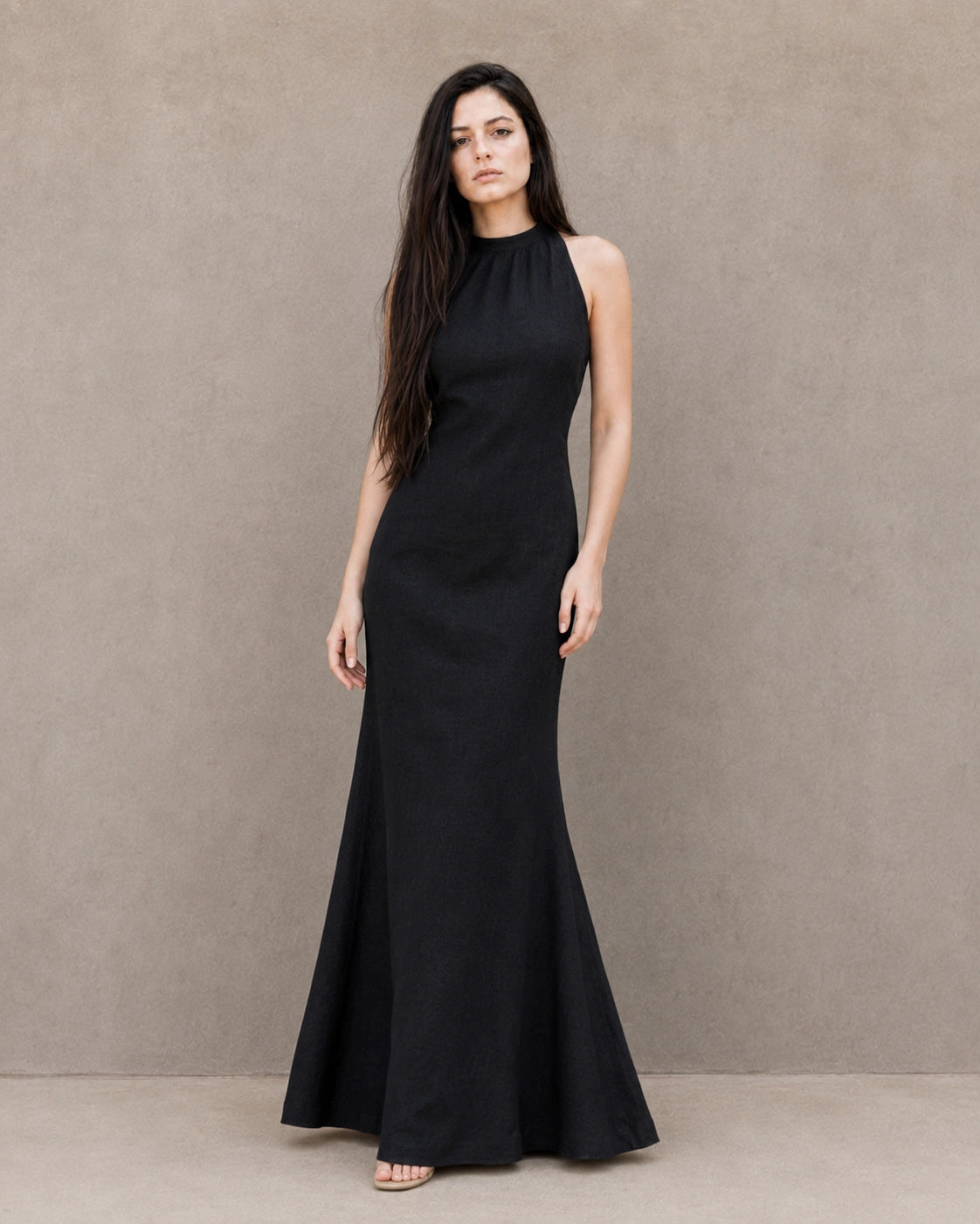 Vrouw draagt een mouwloze linnen jurk in zwart met hoge ronde hals en bias-geknipte A-lijn rok, vooraanzicht.
