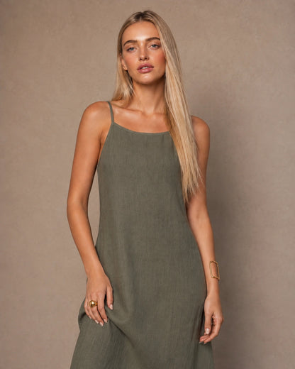 Close-up of a woman wearing an army green cotton-linen halter dress with thin adjustable straps and a square neckline.