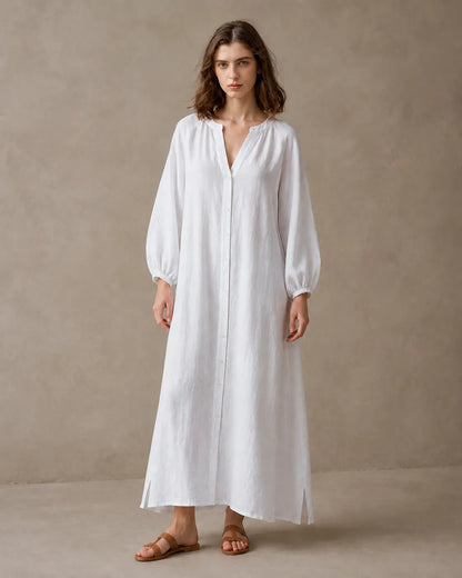 Woman wearing a white cotton-linen dress with a V-neckline, long balloon sleeves with elastic cuffs and a button placket, shown from the front.