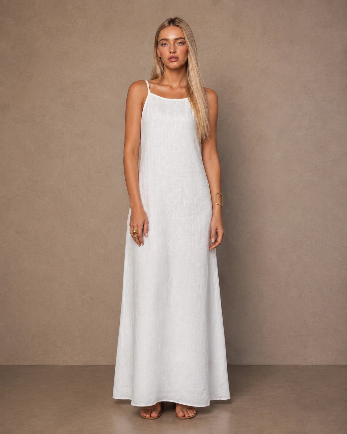 Woman wearing a white cotton-linen halter dress with thin adjustable straps and a flowing A-line skirt, shown from the front.