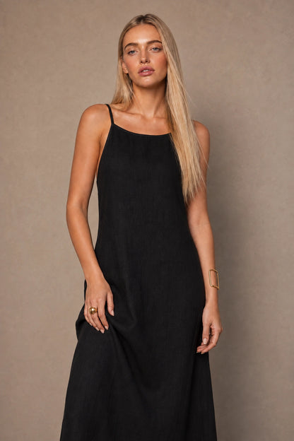 Close-up of a woman wearing a black cotton-linen halter dress with thin adjustable straps and a square neckline.
