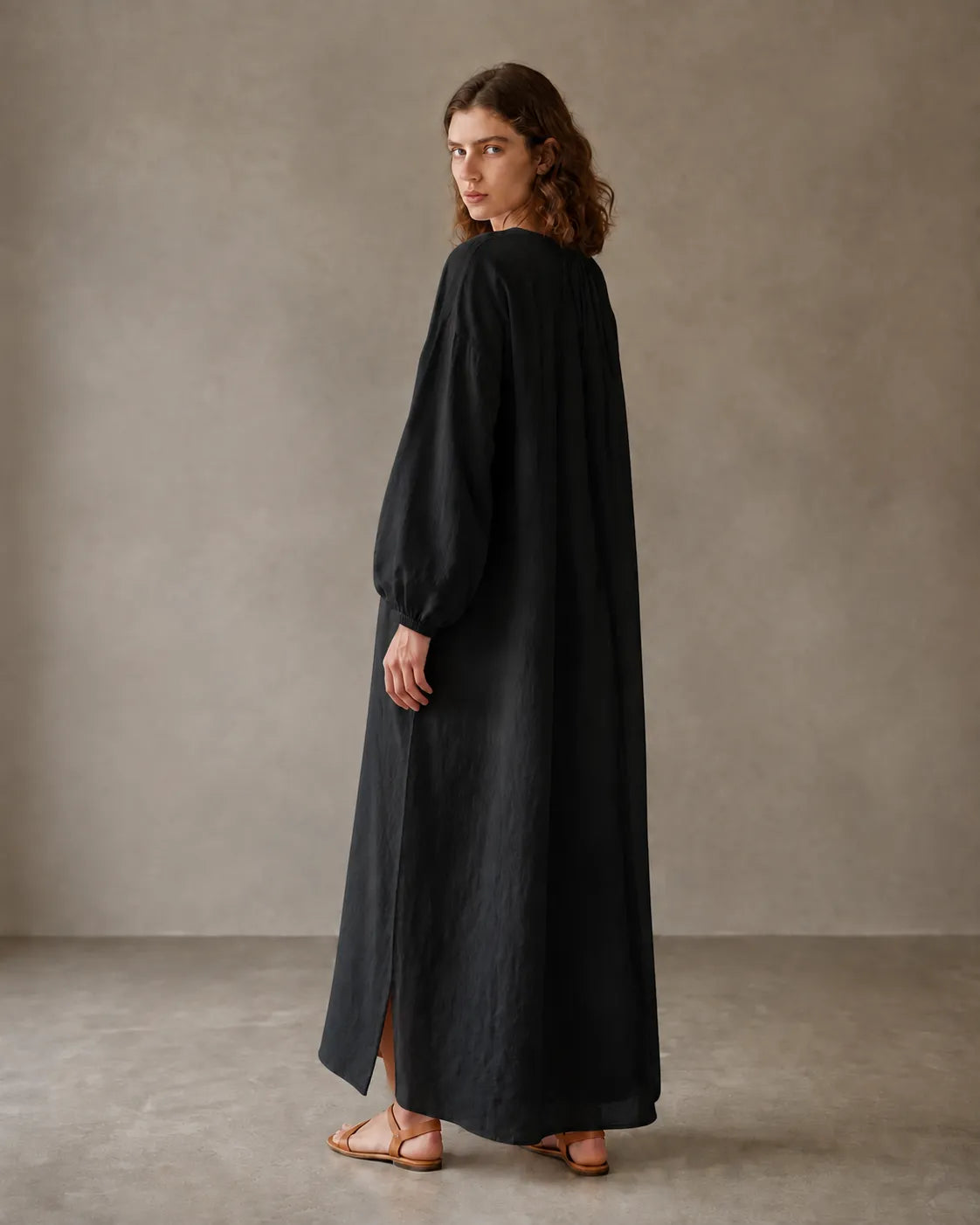 Back view of a black cotton-linen dress with long sleeves and a side hem slit, shown on a model.