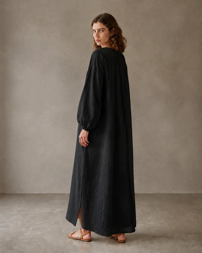 Back view of a black cotton-linen dress with long sleeves and a side hem slit, shown on a model.