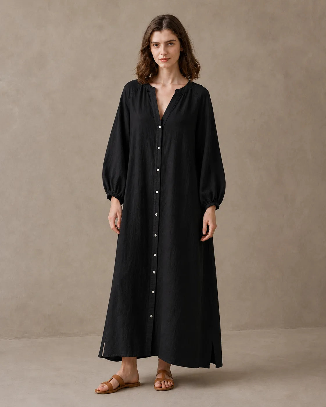 Woman wearing a black cotton-linen dress with a V-neckline, long balloon sleeves with elastic cuffs and a button placket, shown from the front.