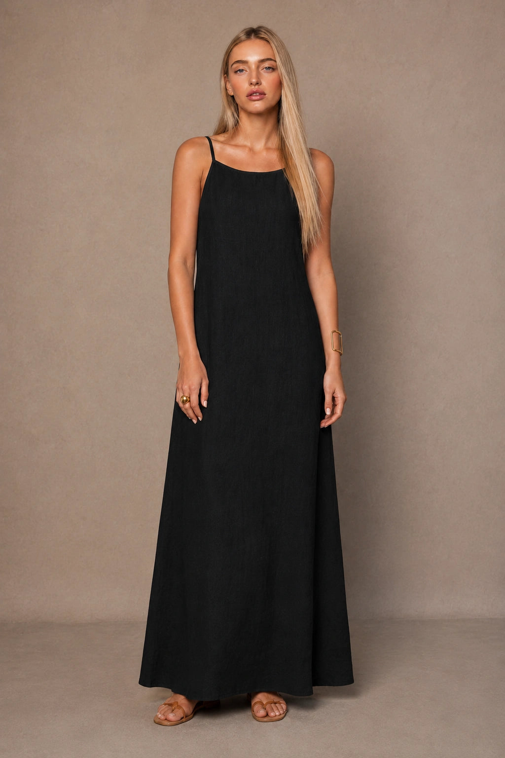 Woman wearing a black cotton-linen halter dress with thin adjustable straps and a flowing A-line skirt, shown from the front.