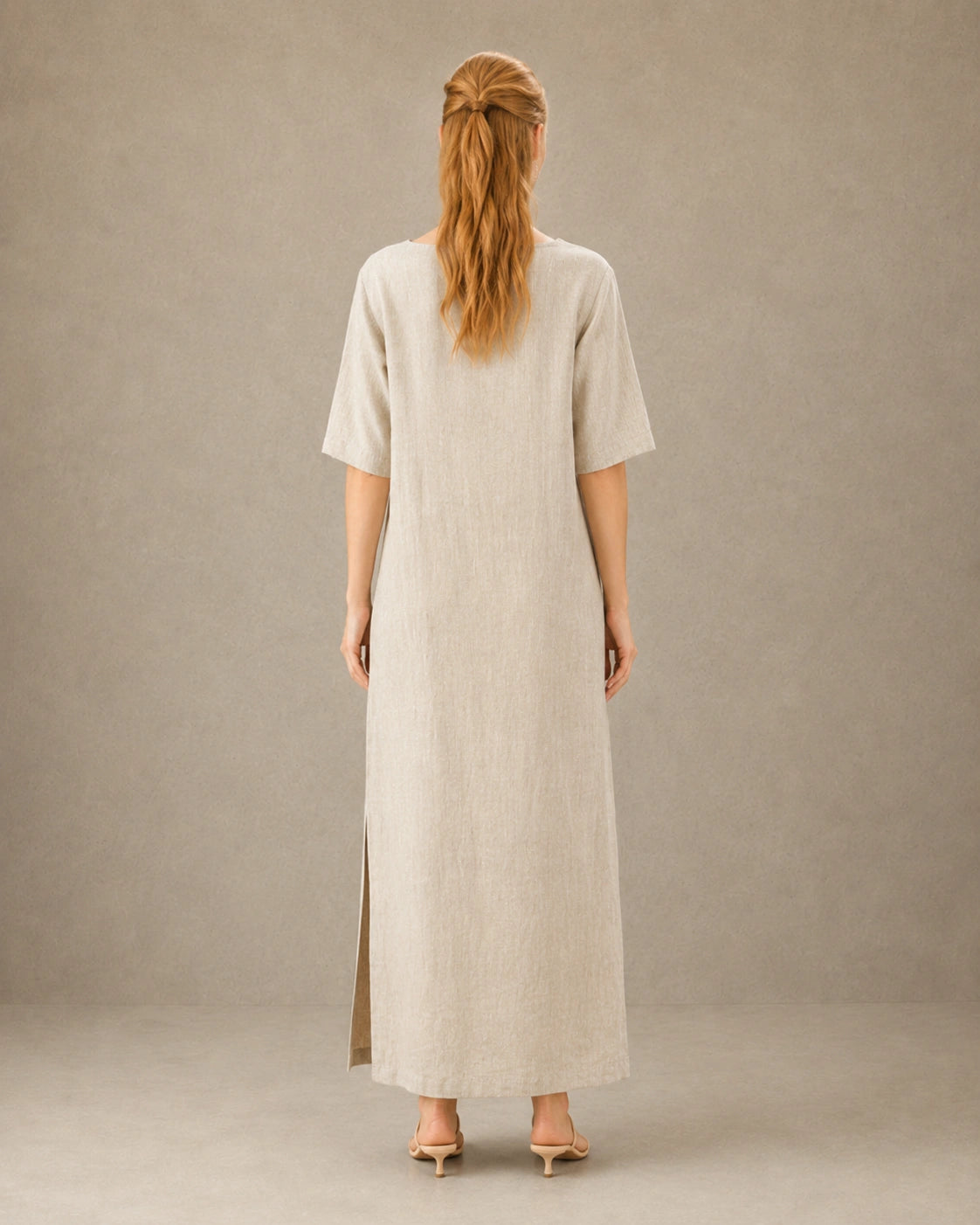 Achteraanzicht van een linnen-tencel jurk in hennep-beige met mouwen tot de elleboog, gedragen door een model.