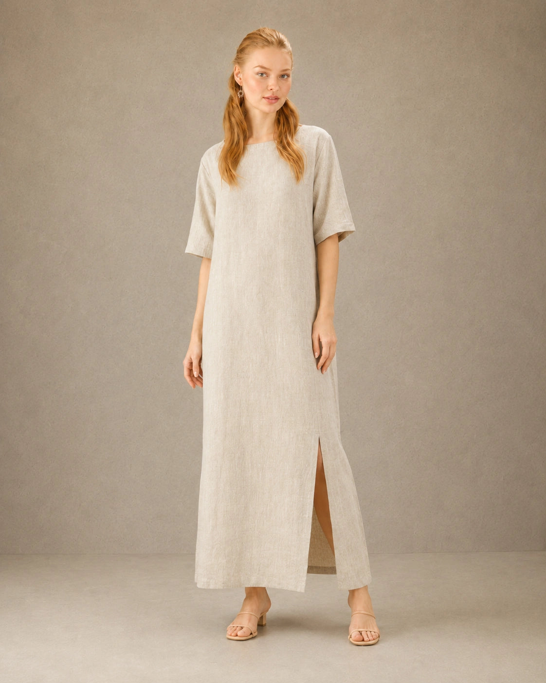 Vrouw draagt een linnen-tencel jurk in hennep-beige, met zicht op de split in de zijzoom, vooraanzicht.
