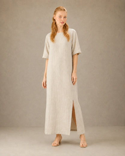 Vrouw draagt een linnen-tencel jurk in hennep-beige, met zicht op de split in de zijzoom, vooraanzicht.