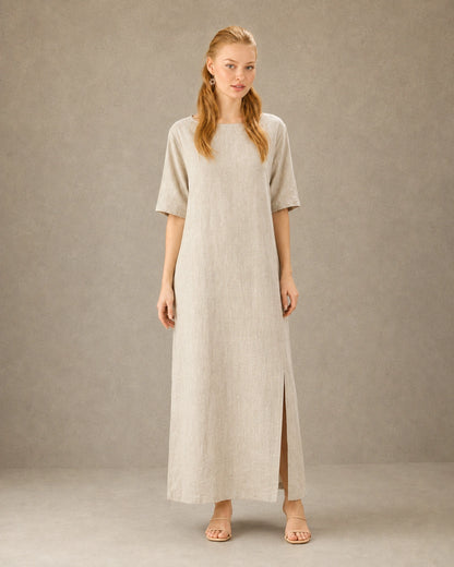 Vrouw draagt een linnen-tencel jurk in hennep-beige met ronde hals, mouwen tot de elleboog en een split in de zijzoom, vooraanzicht.