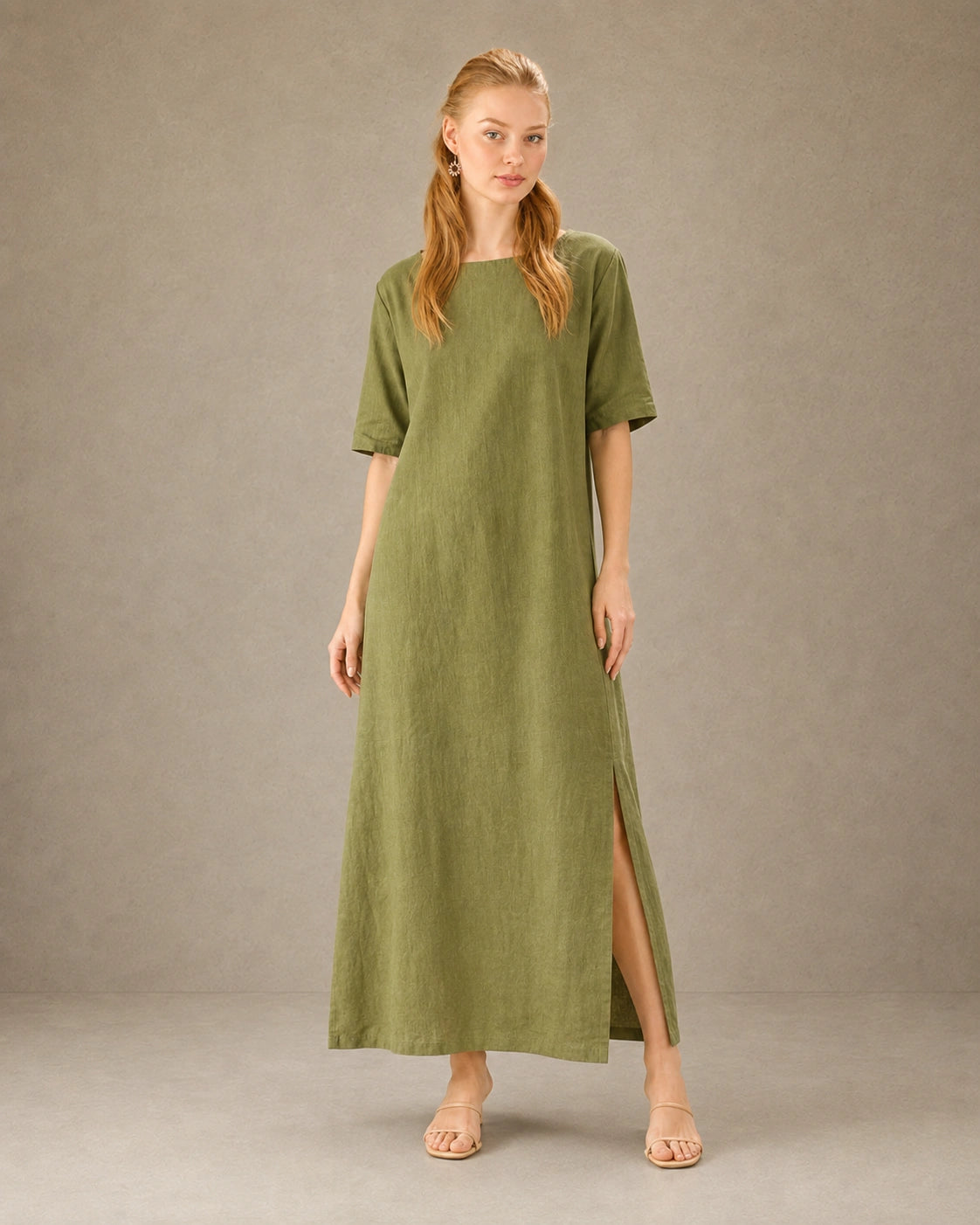 Vrouw draagt een linnen-tencel jurk in mosterdgroen, met zicht op de split in de zijzoom, vooraanzicht.