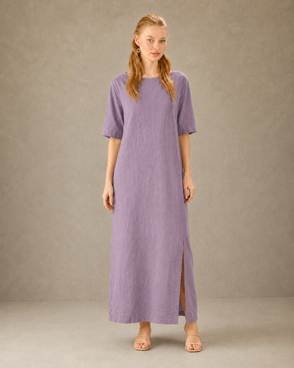 Vrouw draagt een linnen-tencel jurk in paars met ronde hals, mouwen tot de elleboog en een split in de zijzoom, vooraanzicht.