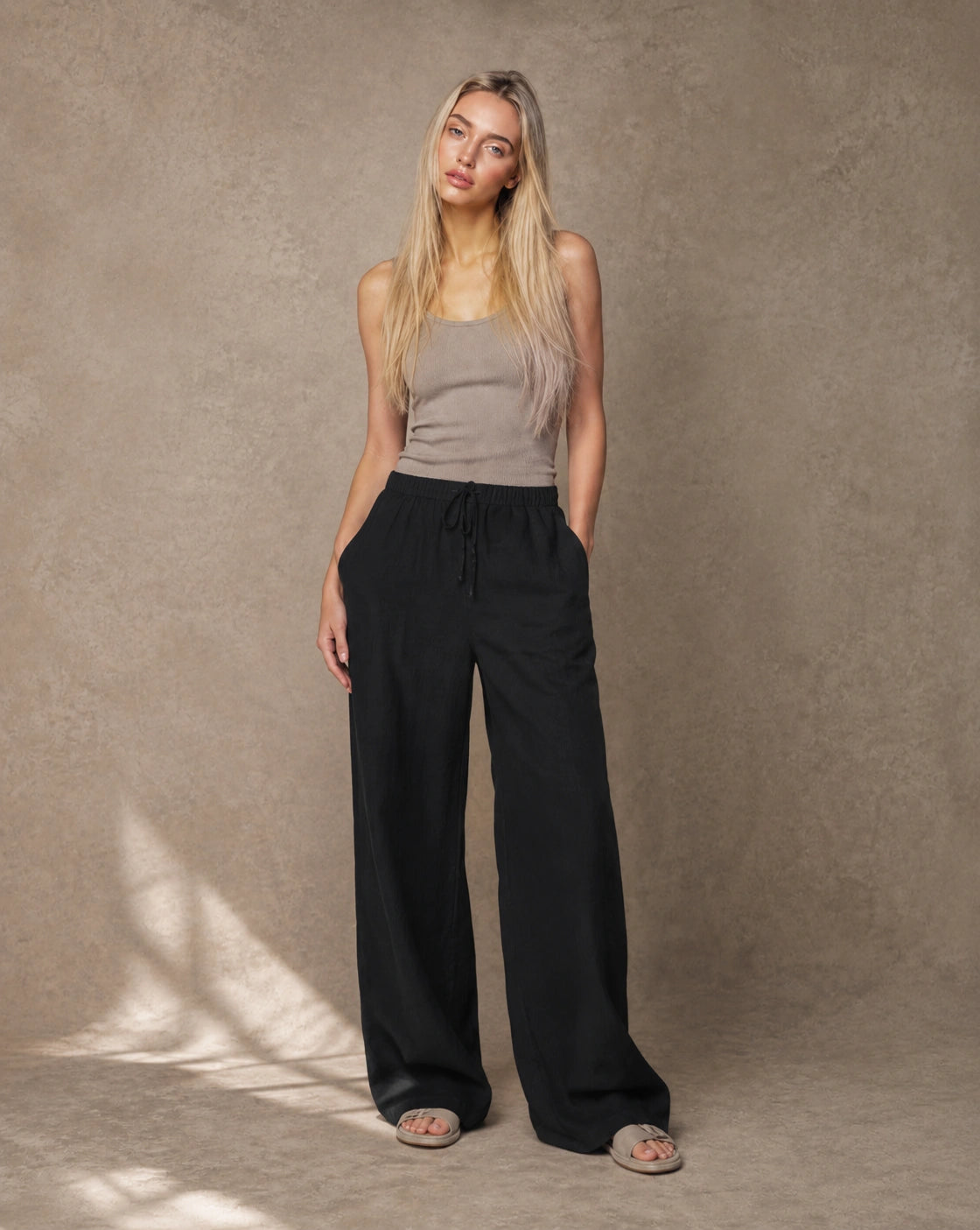 Model draagt een zwarte hoge taille pantalon dames in katoen-linnen-viscosemix met elastische trekkoordtaille, gestyled met een taupe topje, vooraanzicht.