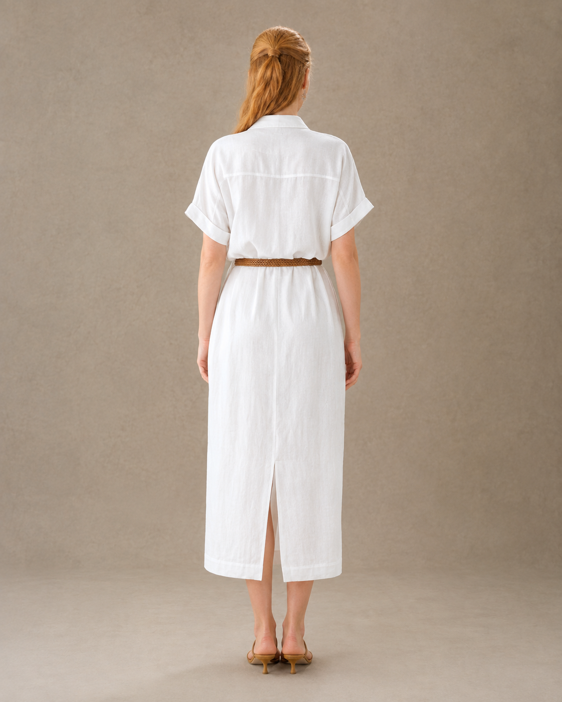 Achteraanzicht van een A-lijn jurk in flax tencel-katoen met gevlochten bruinlederen ceintuur en split in de achterzoom, gedragen door een model.