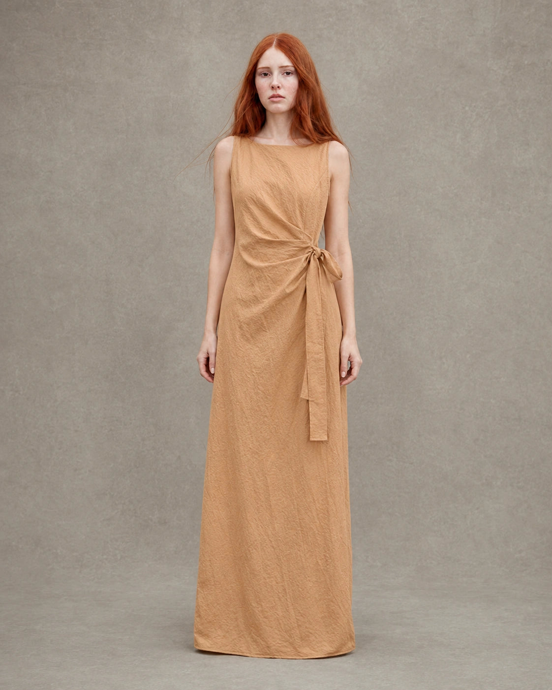 Close-up of a woman wearing an orange tencel-linen dress, showing the gathered waist with a fabric tie and knot detail.