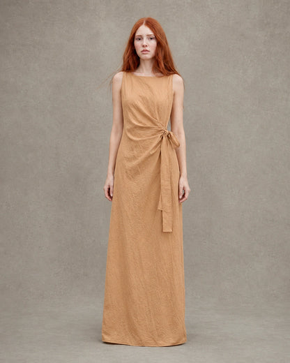 Close-up of a woman wearing an orange tencel-linen dress, showing the gathered waist with a fabric tie and knot detail.